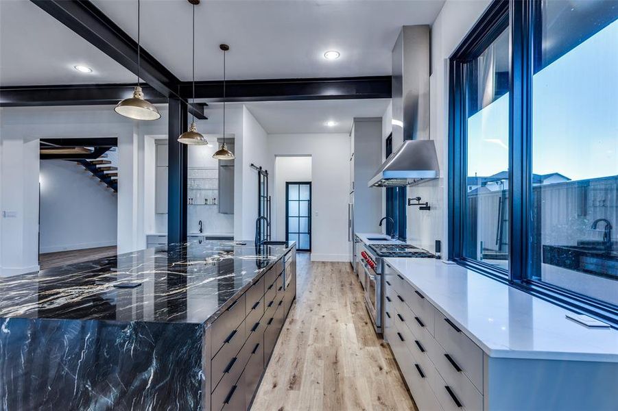 Kitchen with high end range, dark stone counters, wall chimney exhaust hood, hanging light fixtures, and a large island