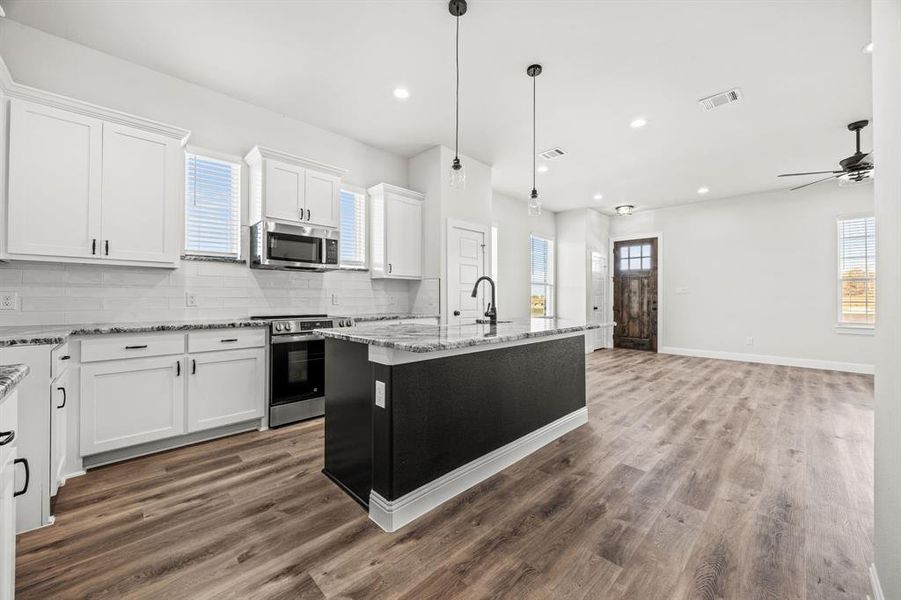 Kitchen featuring stainless steel appliances, a wealth of natural light, a center island with sink, and white cabinets