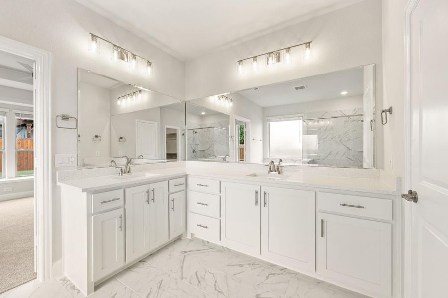 Master bathroom with dual vanities, white cabinets, quartz countertops, and marble tile floors