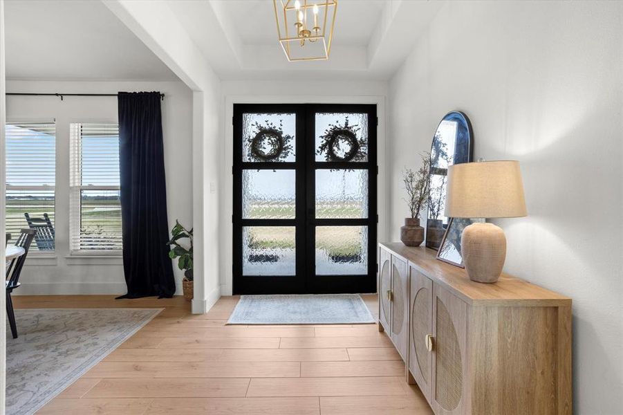 Entrance foyer featuring a chandelier, light wood-type flooring, a tray ceiling, and french doors