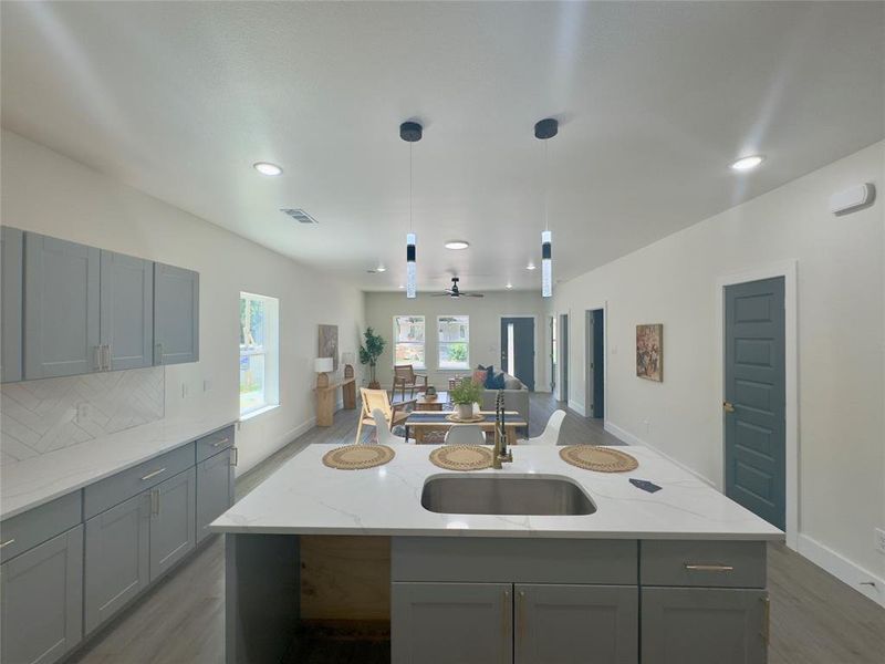 Kitchen featuring hanging light fixtures, light stone countertops, a center island with sink, and sink