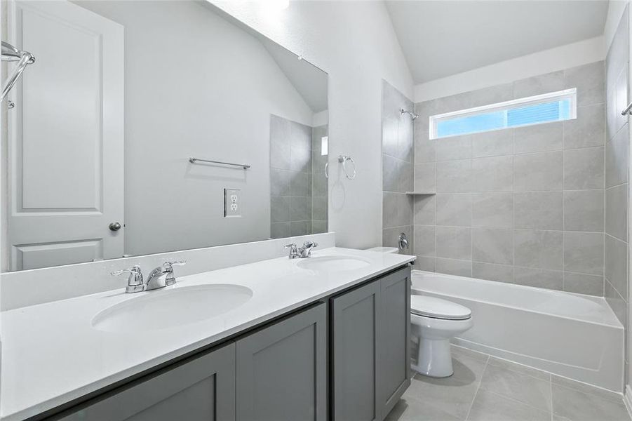 Full bathroom featuring double vanity, vaulted ceiling, shower / tub combination, and light tile patterned floors