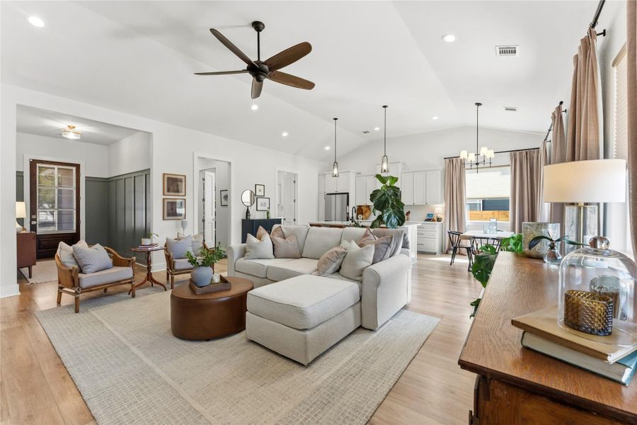 Living room featuring a chandelier, ceiling fan, light wood-style flooring, and lofted ceiling