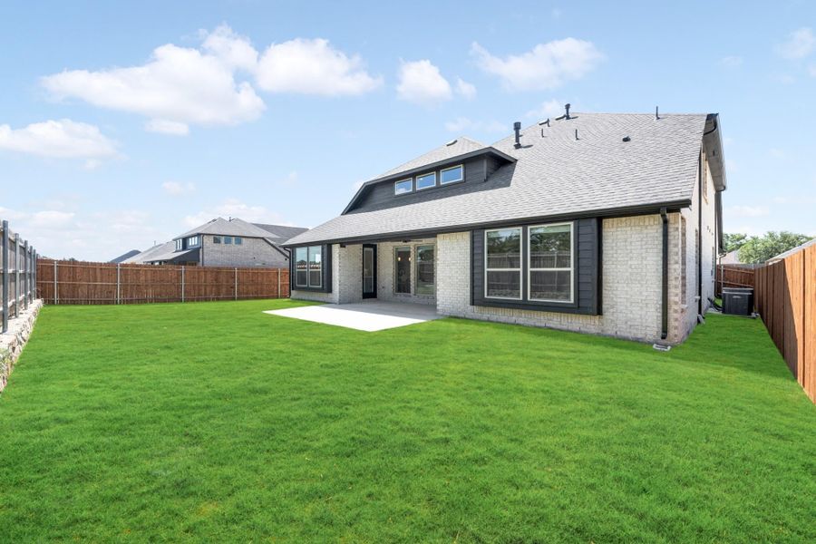 Rear exterior of brick home with large green backyard, concrete patio, and wood privacy fence