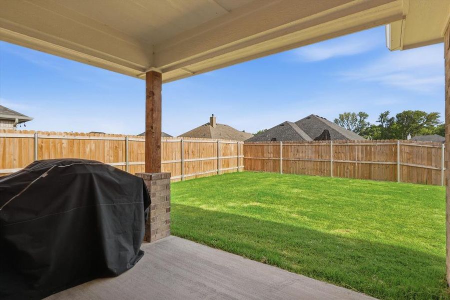 Covered back patio overlooking a fenced grassy backyard, perfect for relaxing, entertaining, and outdoor enjoyment.