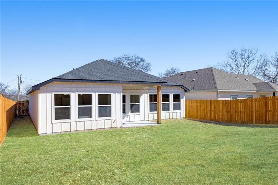 Rear view of house featuring board and batten siding, a fenced backyard, a yard, and a shingled roof