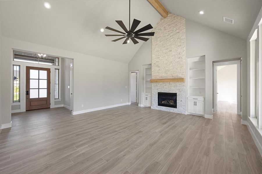 Living room featuring a vaulted ceiling with a beam, built-in shelves & cabinets, ceiling fan, and a stone gas fireplace