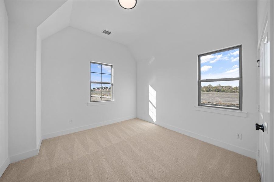 Empty room featuring light colored carpet and vaulted ceiling
