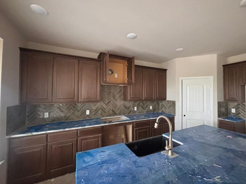 Kitchen featuring dark wood-finish cabinetry, herringbone tile backsplash, an undermount sink with a brushed nickel faucet, and recessed ceiling lighting