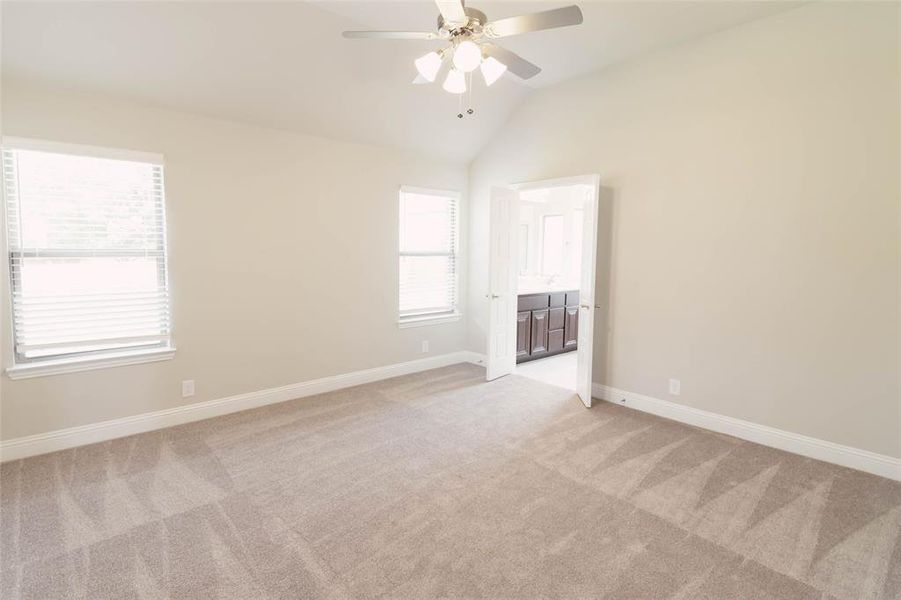 Carpeted primary suite with lofted ceiling and ceiling fan