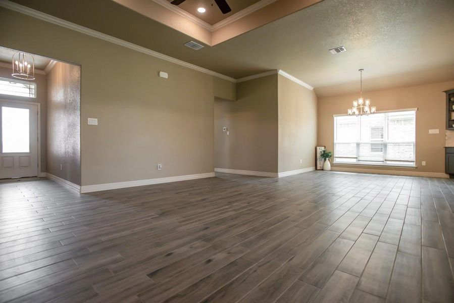 Spare room featuring a chandelier, dark wood finished floors, plenty of natural light, a ceiling fan, and ornamental molding Spare room featuring a chandelier, dark wood finished floors, plenty of natural light, a ceiling fan, and ornamental molding