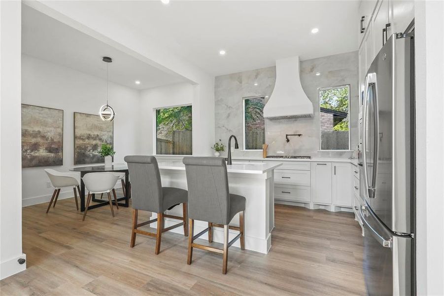 Kitchen featuring decorative light fixtures, white cabinets, freestanding refrigerator, a breakfast bar, and recessed lighting