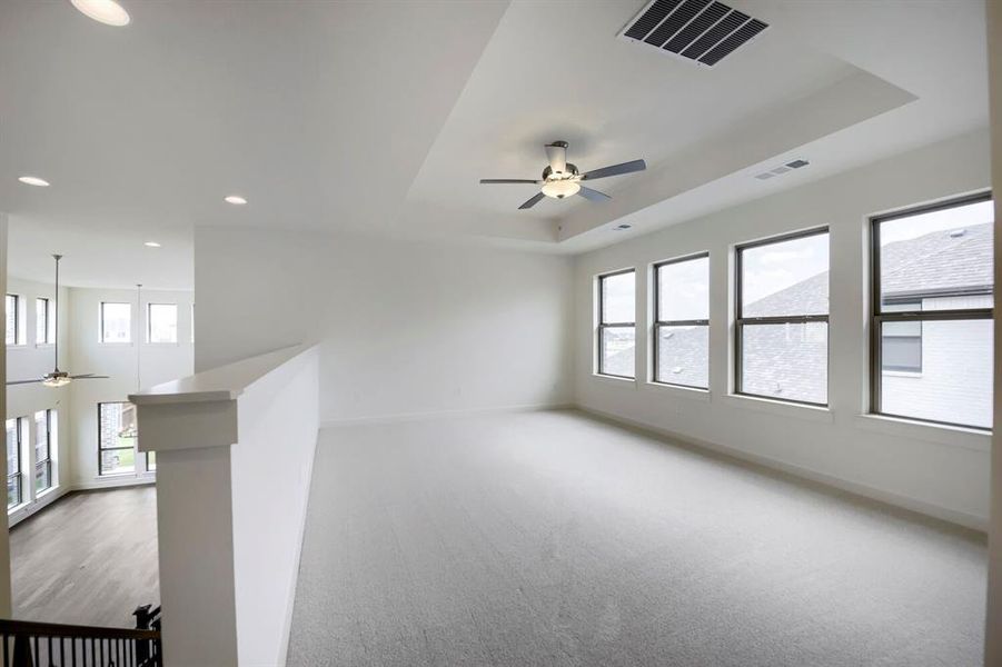 Spacious upper-level area featuring a tray ceiling with a ceiling fan and recessed lighting, multiple windows, and light-toned carpeting Spacious upper-level area featuring a tray ceiling with a ceiling fan and recessed lighting, multiple windows, and light-toned carpeting