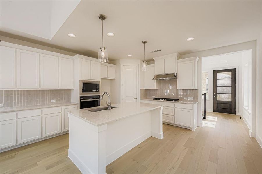 Kitchen with light wood-type flooring, hanging light fixtures, white cabinetry, black oven, and recessed lighting