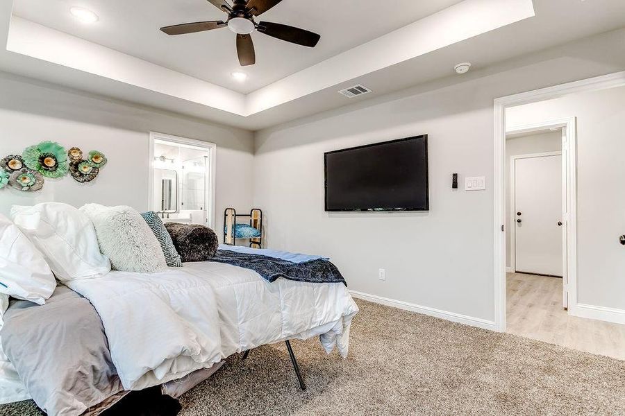 Carpeted bedroom with a tray ceiling, ceiling fan, and ensuite bathroom