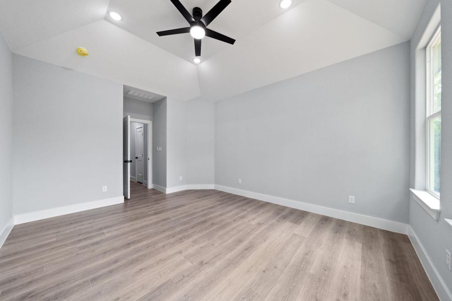 Spacious room featuring vaulted ceilings, recessed lighting, a ceiling fan, wood-finish flooring, and natural light from the window