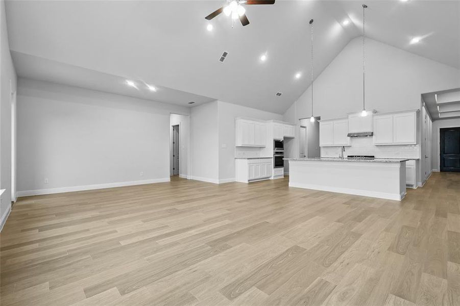 Unfurnished living room featuring high vaulted ceiling, ceiling fan, baseboards, and light wood-type flooring Unfurnished living room featuring high vaulted ceiling, ceiling fan, baseboards, and light wood-type flooring