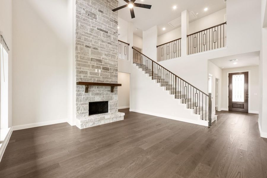 Open living room with two-story stone fireplace, hardwood floors, and staircase with iron railing