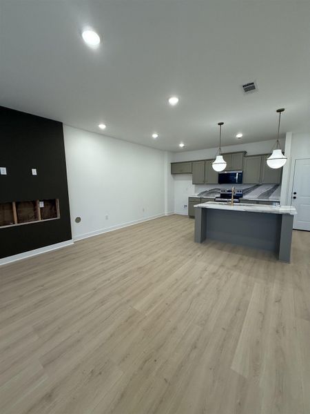 Kitchen featuring gray cabinetry, light wood-style floors, decorative light fixtures, stainless steel appliances, and open floor plan