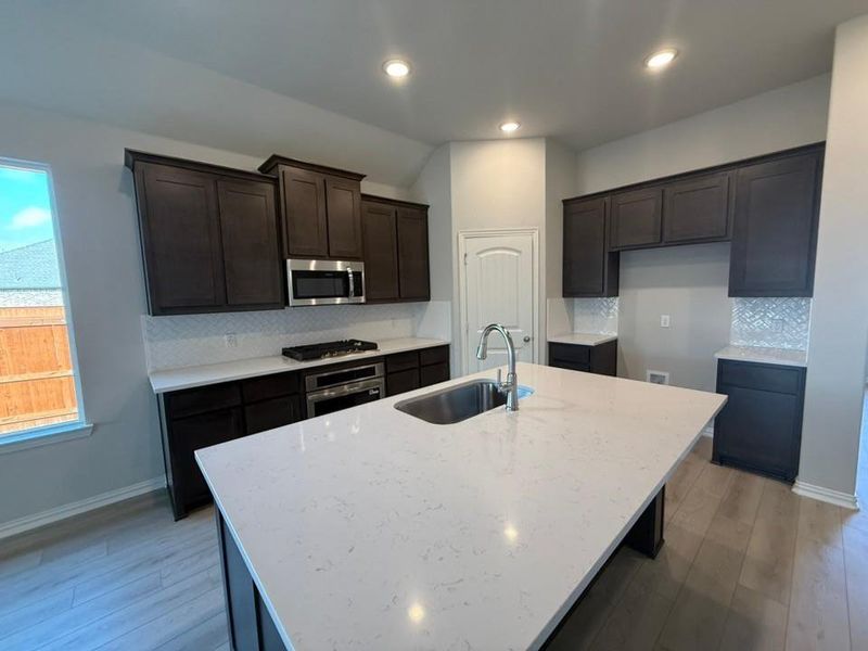 Kitchen with tasteful backsplash, light stone counters, appliances with stainless steel finishes, light wood finished floors, and recessed lighting Kitchen with tasteful backsplash, light stone counters, appliances with stainless steel finishes, light wood finished floors, and recessed lighting