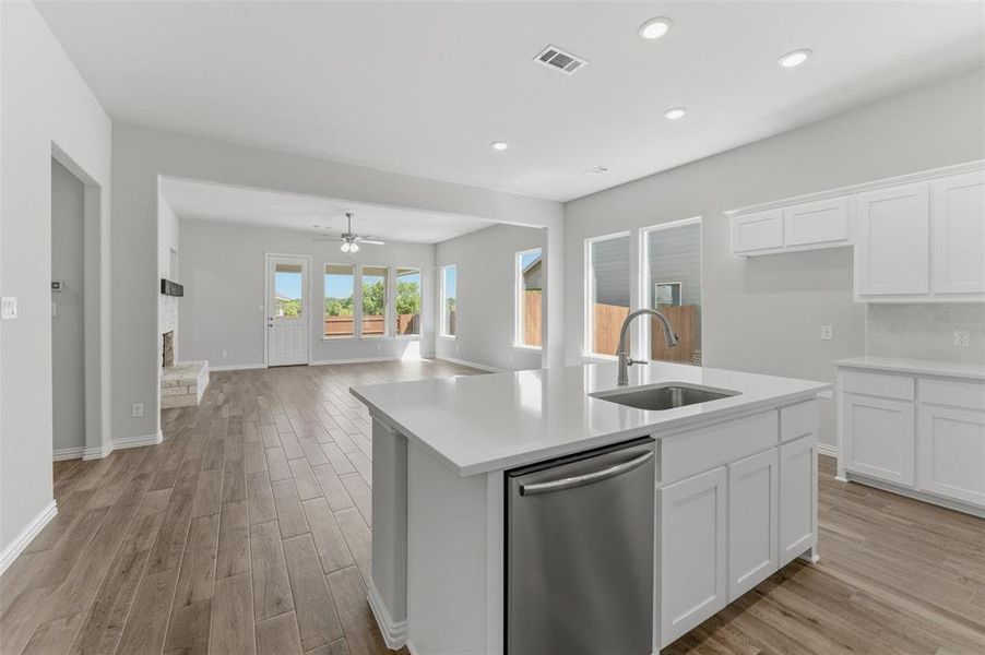 Kitchen featuring stainless steel dishwasher, light wood-style flooring, an island with sink, white cabinetry, and open floor plan