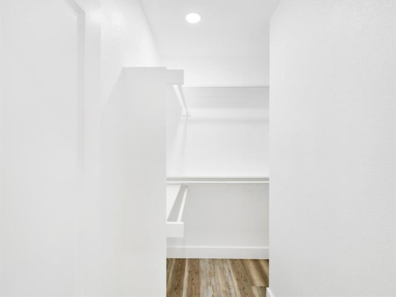 Walk-in closet featuring white walls, recessed lighting, built-in shelving, hanging rods, and wood-finish flooring Walk-in closet featuring white walls, recessed lighting, built-in shelving, hanging rods, and wood-finish flooring