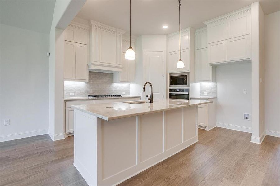 Kitchen with tasteful backsplash, black appliances, an island with sink, sink, and light hardwood / wood-style floors