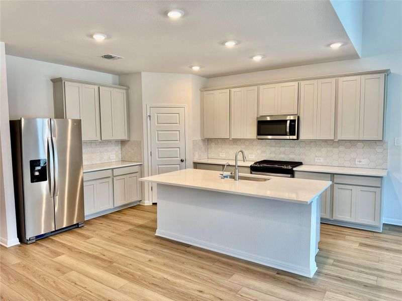 Kitchen featuring appliances with stainless steel finishes, backsplash, light stone counters, light wood-style flooring, and recessed lighting Kitchen featuring appliances with stainless steel finishes, backsplash, light stone counters, light wood-style flooring, and recessed lighting