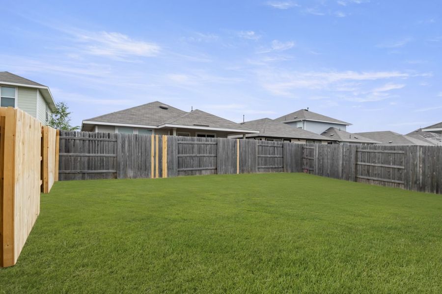 Image of the backyard of a two story home with green grass and wooden fence