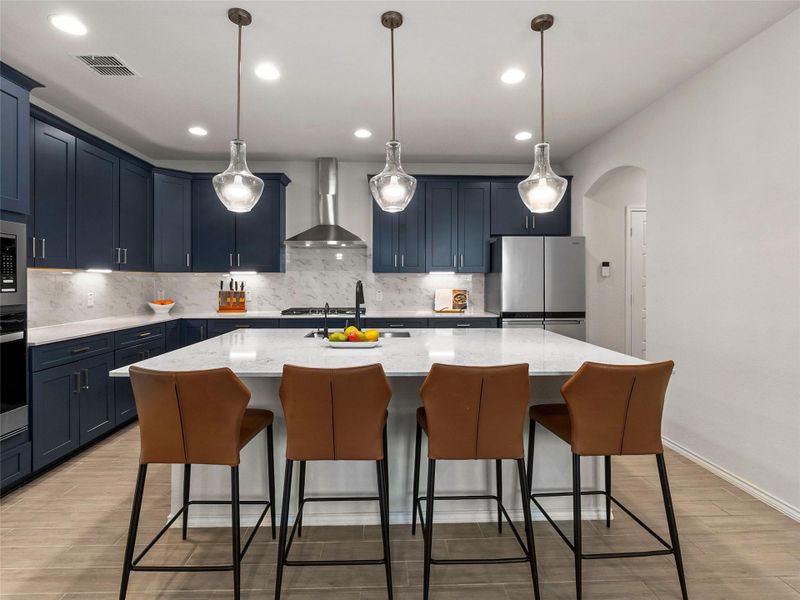 Kitchen with arched walkways, light stone counters, a breakfast bar area, a center island with sink, and blue cabinets