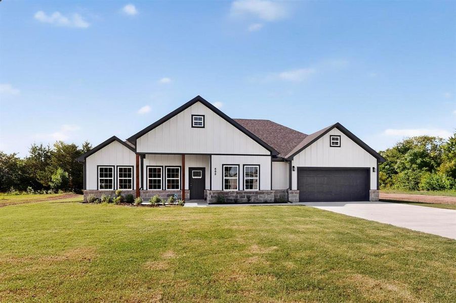 Modern farmhouse featuring board and batten siding, a front lawn, driveway, stone siding, and an attached garage Modern farmhouse featuring board and batten siding, a front lawn, driveway, stone siding, and an attached garage