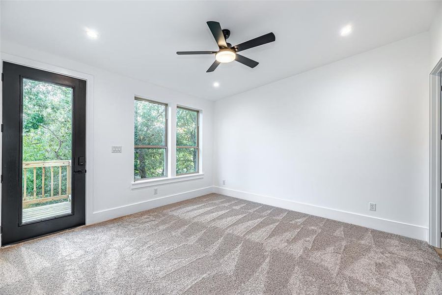 Bright, spacious primary bedroom with plush carpeting, multiple windows offering natural light, a modern ceiling fan, and direct access to an outdoor deck through a glass door.