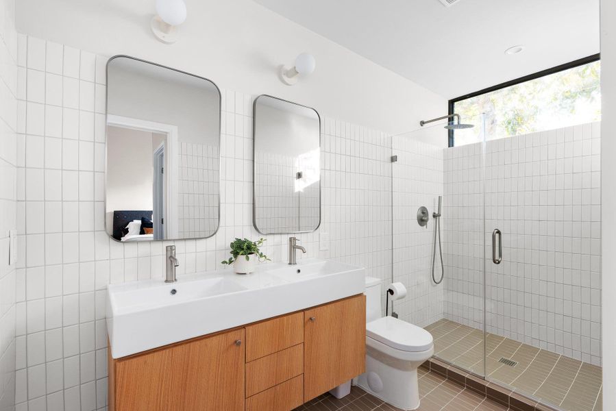 Bathroom with double vanity, tile walls, a shower stall, dark tile patterned flooring, and decorative backsplash Bathroom with double vanity, tile walls, a shower stall, dark tile patterned flooring, and decorative backsplash