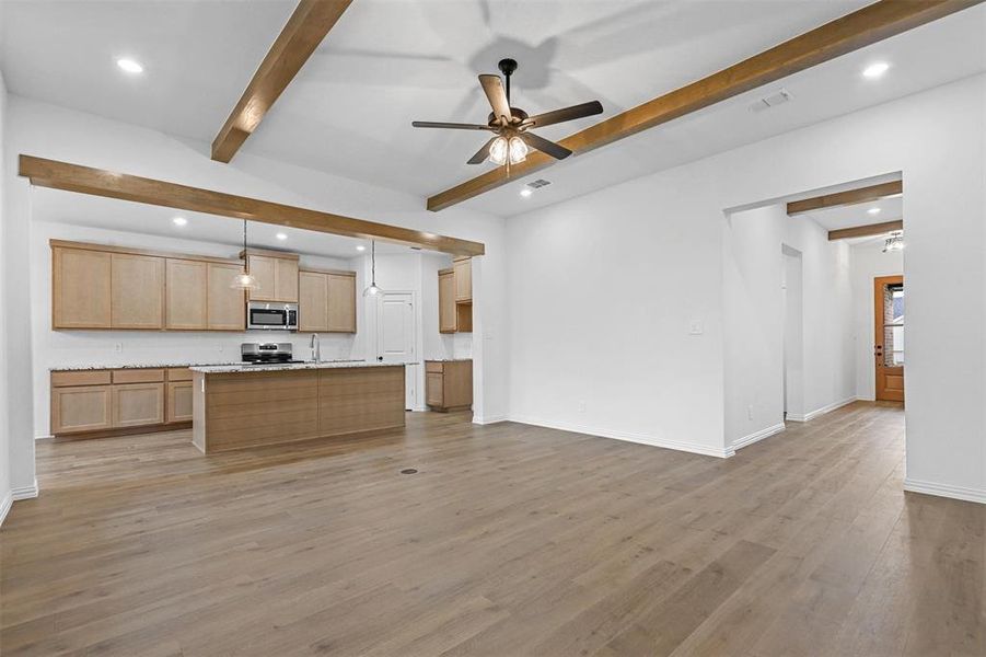 Kitchen featuring stainless steel appliances, a center island, beam ceiling, light wood-type flooring, and decorative light fixtures