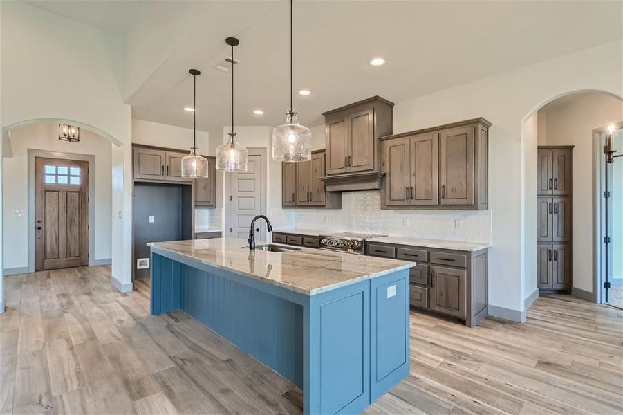 Kitchen with stainless steel range, light wood-type flooring, sink, decorative backsplash, and a center island with sink