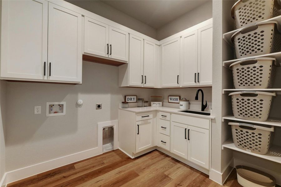 Laundry room featuring white shaker cabinetry, wood-finish flooring, white countertops, a black sink, a black gooseneck faucet, and built-in shelving