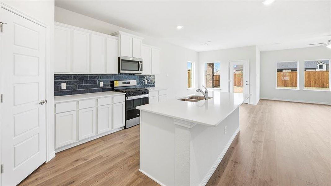Kitchen featuring stainless steel appliances, white cabinets, a kitchen island with sink, backsplash, and light wood-type flooring