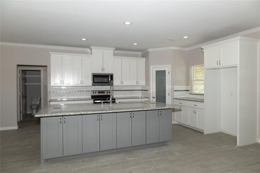 Kitchen with light stone countertops, backsplash, white cabinets, a kitchen island with sink, and appliances with stainless steel finishes