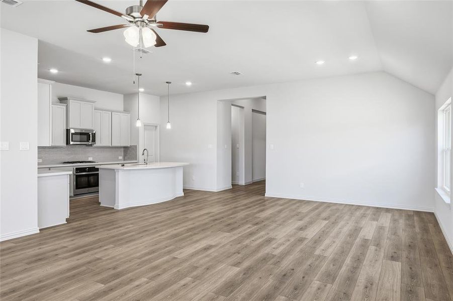 Kitchen with ceiling fan, a kitchen island with sink, open floor plan, white cabinetry, and stainless steel appliances