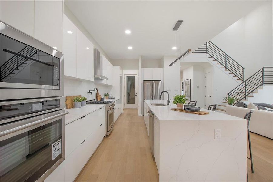 Kitchen with light hardwood / wood-style flooring, hanging light fixtures, sink, white cabinetry, and appliances with stainless steel finishes