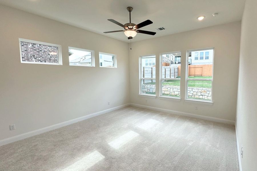 A well-lit bedroom features plush carpeting and multiple windows.