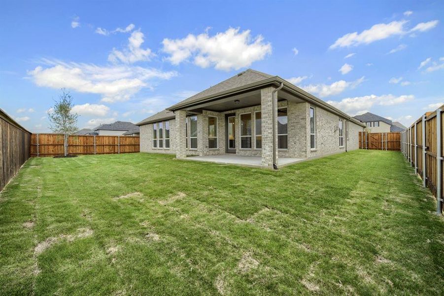 Expansive grassy backyard featuring a covered patio, brick exterior, and full wood fencing Expansive grassy backyard featuring a covered patio, brick exterior, and full wood fencing