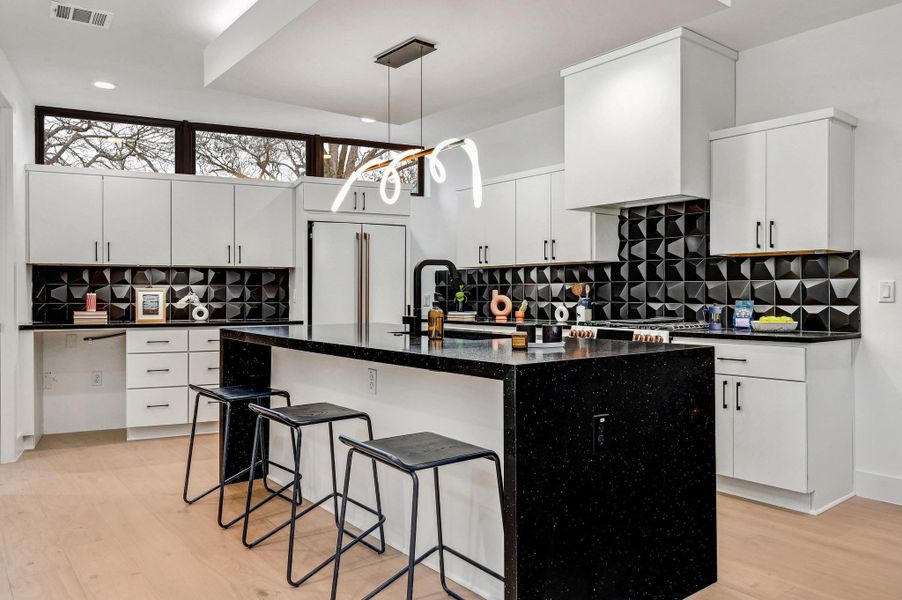 Kitchen featuring a kitchen bar, backsplash, a center island with sink, dark stone counters, and white cabinetry