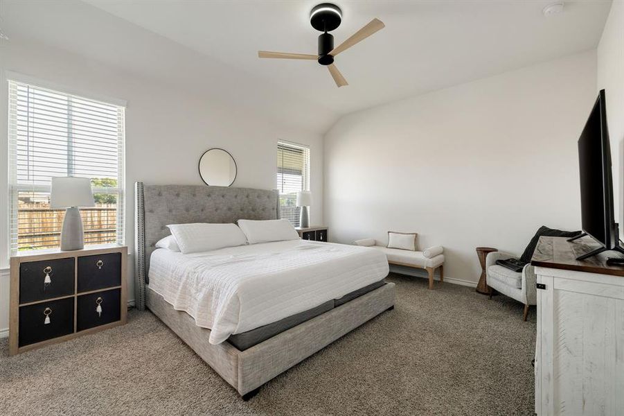 Carpeted bedroom featuring vaulted ceiling, multiple windows, and a ceiling fan Carpeted bedroom featuring vaulted ceiling, multiple windows, and a ceiling fan
