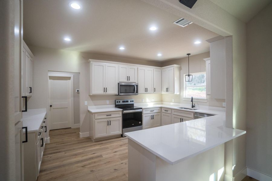 Kitchen with visible vents, a sink, appliances with stainless steel finishes, a peninsula, and light wood finished floors