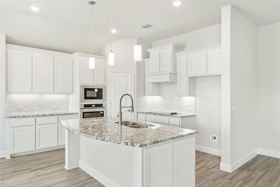 Kitchen with white cabinets, granite island with sink, pendant lights, and hardwood floors