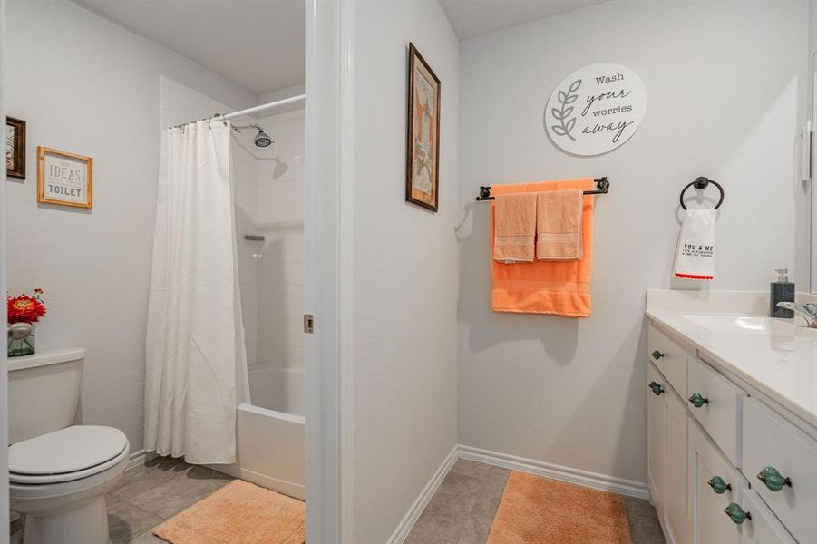 Full bath with vanity, shower / bathtub combination with curtain, baseboards, tile patterned flooring, and toilet