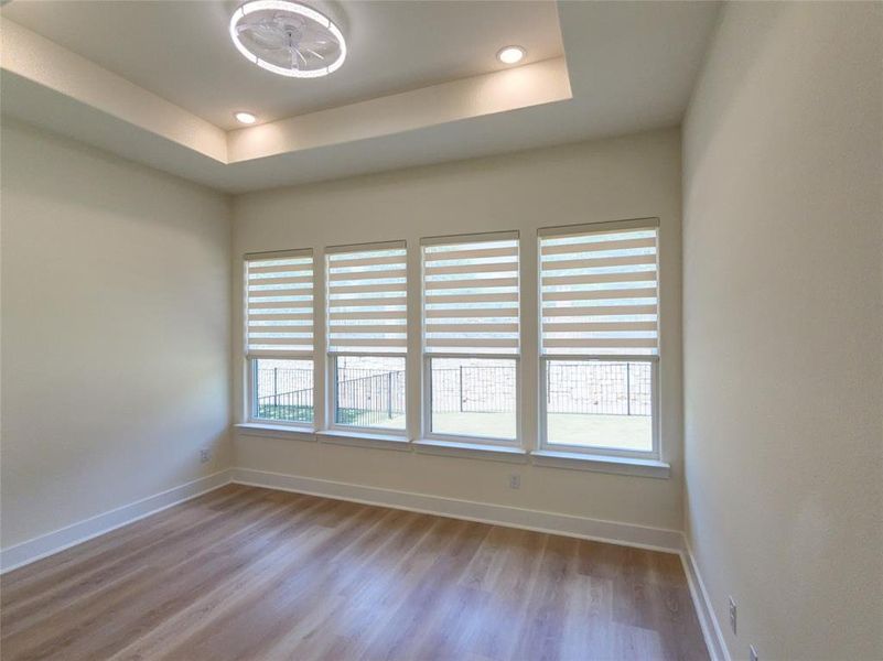 Neutral-toned interior featuring wood-finish flooring, a tray ceiling with recessed lighting, and a modern ceiling fan