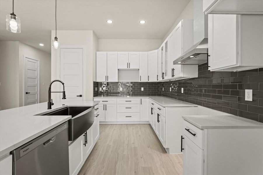 Kitchen with white cabinets, stainless steel dishwasher, backsplash, hanging light fixtures, and light wood finished floors Kitchen with white cabinets, stainless steel dishwasher, backsplash, hanging light fixtures, and light wood finished floors