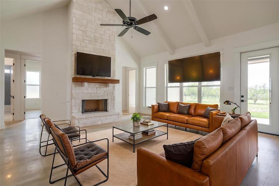 Living room with a stone fireplace, a ceiling fan, high vaulted ceiling, and beam ceiling